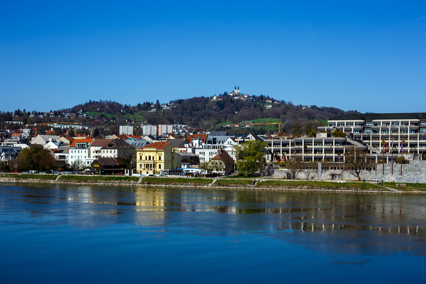 Blick bei der Nibelungenbrücke in Linz am 04 April 2025 über die Donau auf den 539 m hohen Pöstlingberg, worauf die barocken Wallfahrtskirche Pöstlingberg thront. 

Er ist ein beliebtes Ausflugsziel mit der Pöstlingbergbahn, mit der Aussichtsplattform auf die Stadt Linz, der barocken Wallfahrtskirche Pöstlingberg und der Linzer Grottenbahn. 