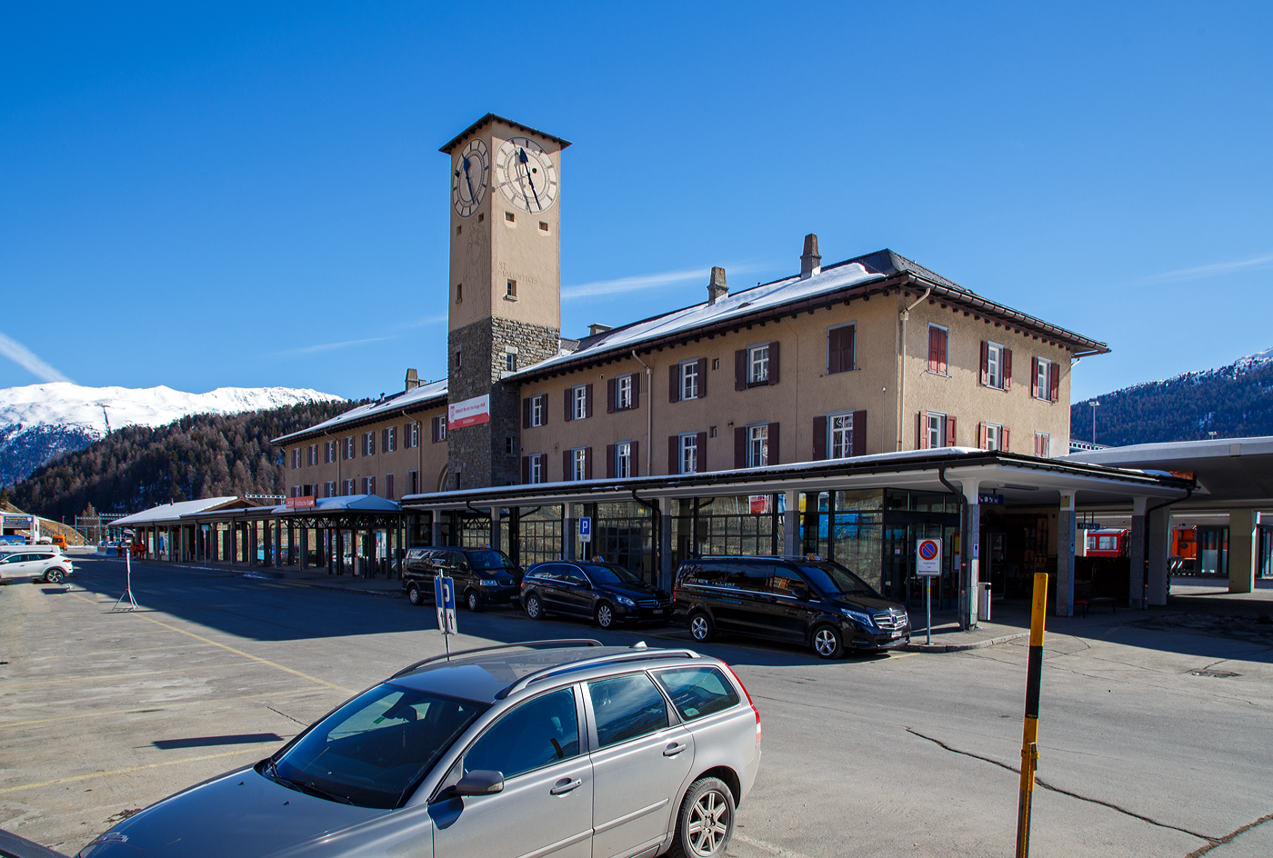 Der RhB Bahnhof St. Moritz blick von der Vorplatzseite mit dem Empfangsgebäude und links dem Güterschuppen am 20 Februar 2017. 

Der Bahnhof St. Moritz ist der Bahnhof des Kurortes St. Moritz im Oberengadin im Kanton Graubünden. St. Moritz ist nach dem heiligen Mauritius benannt, der auch im Wappen abgebildet ist. Er ist aber auch hier an den Uhrenturm abgebildet. Der Bahnhof wird von der Rhätischen Bahn (RhB) betrieben und liegt auf 1.775 m über Meer am nordwestlichen Hang des Tales unmittelbar oberhalb des St. Moritzersees beim Ausfluss des Inn. Er ist Endbahnhof der Albulabahn und der Berninabahn. Da diese mit unterschiedlichen Stromsystemen betrieben werden, ist er zugleich ein Systemwechselbahnhof.

Hinten links sieht man auch die Standseilbahn Muottas-Muragl-Bahn (MMB). Die Standseilbahn führt von Punt Muragl (1.739 m ü. M.) zwischen Samedan und Pontresina, auf den Muottas Muragl (2.448 m ü. M.). Die Bahn hat eine Streckenlänge von 2.199 m und überwindet eine Höhendifferenz  von 709 m. Sie ist die älteste Bergbahn im Engadin und feierte 2007 ihr 100-jähriges Bestehen.

Der Bahnhof St. Moritz:
Der Bahnhof wurde als Durchgangsbahnhof gebaut, da anfänglich eine Verlängerung der Strecke Richtung Maloja geplant war. So führte ein Gleis von der Westseite des Bahnhofs zunächst über eine Brücke und anschließend fast in den Hang hinein. An dieser Stelle war das Portal eines Tunnels geplant, der das Ortszentrum von St. Moritz unterfahren sollte.

Im Hinblick auf die Skiweltmeisterschaften 2017 in St. Moritz wurde der Bahnhof zwischen 2014 und 2017 zu einem Kopfbahnhof mit schienenfreien Zugängen und einem Querperron ausgebaut. Die drei neuen, überdachten Perrons (Bahnsteige) an fünf Personengleisen sind behindertengerecht gestaltet. Wobei die alte Gestaltung mir persönlich besser gefiel. Das Bahnhofgebäude blieb unverändert, während der Bahnhofplatz mit einem Busterminal neu konzipiert wurde. Der Güterschuppen wird für bahneigene Nutzung verwendet. Für die diversen neuen Abstellgleise musste die RhB eine 250m lange Stützmauer entlang der Kantonsstraße erstellen lassen.

Baulich:
Das stattliche Aufnahmegebäude liegt auf der Bergseite der Gleisanlagen und besitzt einen Hausbahnsteig. Dazu existieren ein Mittelbahnsteig für die Züge des RhB-Stammnetzes und ein weiterer für die Züge der Berninabahn. Östlich des Empfangsgebäudes steht der Güterschuppen mit Rampe (hier links im Bild), eine weitere offene Verladerampe liegt im östlichen Bahnhofsteil zwischen den beiden Streckenausfahrten. Daneben sind umfangreiche Abstellanlagen vorhanden.

Die Berninabahn führt unmittelbar nach dem Bahnhof über die Innbrücke und kurz darauf in den 689 m langen Charnadüra-Tunnel II. Unter der Bahnbrücke führt eine Straßenbrücke in einem anderen, sich kreuzenden Winkel über den Inn. Die Albulabahn führt gleich nach dem Bahnhof in den 114 m langen Argenteri-Tunnel und kurz darauf durch den 448 m langen Charnadüra-Tunnel I.

Das Empfangsgebäude wurde 1927 gebaut und ersetzte das erste Empfangsgebäude.

Betrieblich:
Der Bahnhof ist betrieblich zweigeteilt, da die beiden Strecken mit unterschiedlichen Stromsystemen betrieben werden. So ist die zum RhB-Stammnetz (StN) gehörende Albulabahn mit 11 kV 16⅔ Hz Wechselstrom, die Berninabahn (BB) dagegen mit 1 kV Gleichstrom elektrifiziert. Für Rangiermanöver waren aus diesem Grund 2017 noch dieselbetriebene Rangierfahrzeuge (z.B. RhB Tm 2/2) stationiert.

Der Fahrplan besteht aus einem stündlichen InterRegio über die Albulabahn nach Chur und einem stündlichen Regio nach Pontresina, der meistens nach Tirano weiterfährt. Der InterRegio hat in Samedan Anschluss an die Züge ins Unterengadin. Zusätzlich verkehren RegioExpress nach Zernez (– Vereinatunnel –) Klosters – Landquart. Der Bahnhof ist der offizielle Start- und Endpunkt des Glacier-Expresses. Aber auch die Triebwagen, die den Bernina-Express führen, starten und enden hier, während die Panoramawagen von und nach Chur beziehungsweise Davos von einem Zweistrom-Triebzug des Typs ABe 8/12 «Allegra» gezogen werden und direkt nach Pontresina fahren.