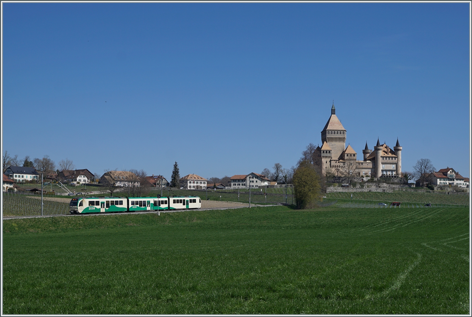 Zwei BAM MBC SURF Be 4/4 mit Mittelwagen sind als Regionalzug von Morges nach Bières kurz vor Vufflens le Château unterwegs. Im Hintergrund ist das Schloss von Vufflens zu sehen.

April 2023